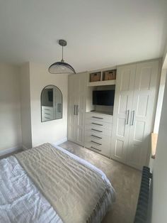 a large bed sitting in a bedroom next to a tall white wall mounted cabinet and mirror