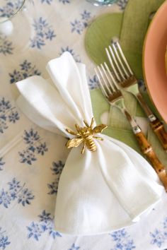 a napkin with a gold bee on it sitting next to a fork and spoons