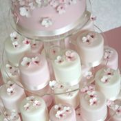 there are many small cakes on the cake stand with pink and white frosting flowers