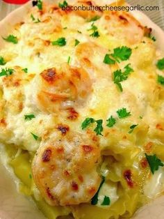 a white plate topped with pasta and shrimp covered in cheese sauce, garnished with parsley