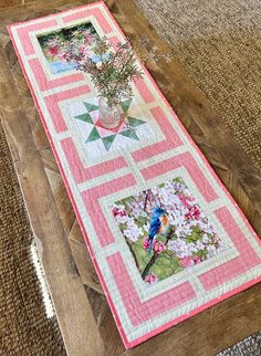 a quilted table runner with flowers in a vase on the top and an image of a bird