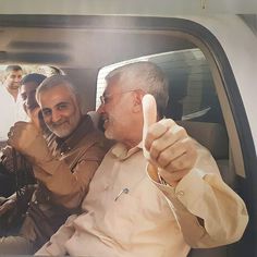 two men sitting in the back seat of a car giving thumbs up while another man stands next to them