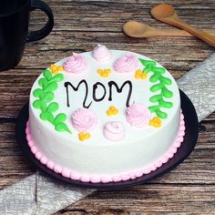 a cake with the word mom written on it next to a cup of coffee and spoons