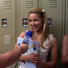 a woman holding a book and microphone in front of lockers