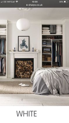 an image of a bedroom with white furniture and clothes on the closet doors, in front of a fireplace