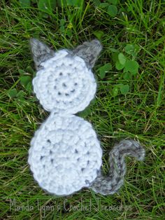 a crocheted cat laying in the grass with it's tail curled up