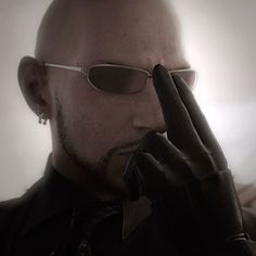 a bald man wearing sunglasses and holding his hand up to his face with both hands