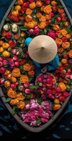 a person in a boat with flowers floating on the water and wearing a straw hat