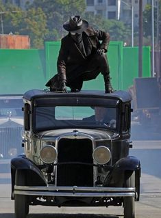 an old fashion car driving down the road with a man in a hat on top