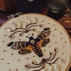 a close up of a embroidery on a piece of cloth with flowers and moths in it