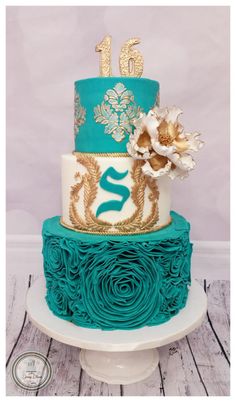 a three tiered blue and gold cake with flowers on top