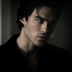 a young man with dark hair and blue eyes stares at the camera while wearing a black shirt