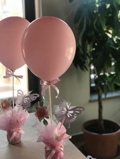 two pink balloons with flowers and butterflies on them sitting on a table next to a potted plant