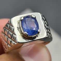 a man's hand holding a ring with a blue stone in the middle of it