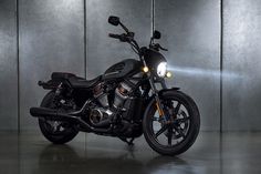 a black motorcycle is parked in front of a gray wall and some lights are on