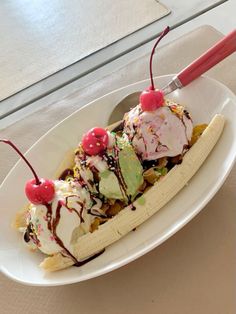 a banana split with ice cream and cherries on top in a white bowl sitting on a table