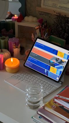 an open laptop computer sitting on top of a desk next to a candle and books