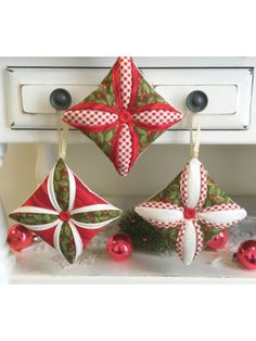 three christmas ornaments hanging from the side of a white stove top with red and green decorations