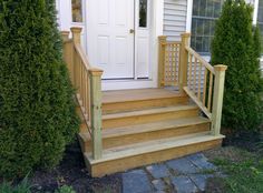 a wooden porch with steps leading up to the front door and two bushes next to it