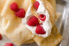 raspberries and whipped cream are on top of crepes