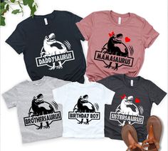 four t - shirts with dinosaurs printed on them and sandals next to plant in the foreground