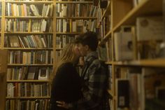 two people standing in front of a book shelf with many books on it and one person kissing the other