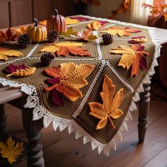 a table topped with a knitted tablecloth covered in leaves and acorns