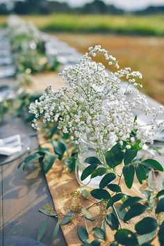 the table is set with several vases filled with baby's breath flowers and greenery