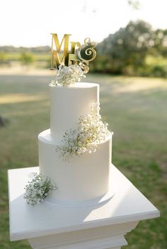 a three tiered white wedding cake with flowers on top and mr and mrs sign