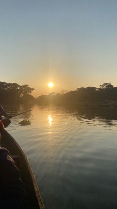 the sun is setting over some water with people in canoes looking out at it