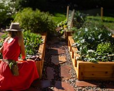 a woman in a red dress and hat sitting on a bench surrounded by garden plants