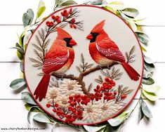 two red birds sitting on top of a tree branch next to leaves and berries in a circle