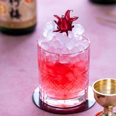 a red drink with ice and garnish on the rim next to a gold cup