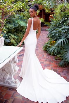 a woman in a white wedding dress standing next to a table with plants on it