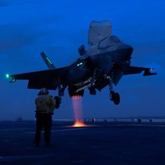 a fighter jet sitting on top of an airport runway next to a man standing in front of it