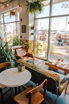 the inside of a restaurant with tables, chairs and potted plants on the windowsill