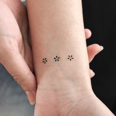 a woman's wrist tattoo with four small flowers on the left side of her arm