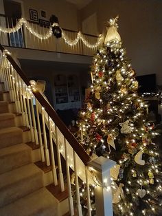 a decorated christmas tree sitting on top of a banister next to a stair case