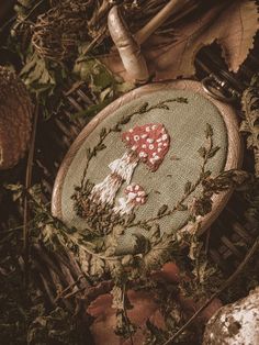 a cross - stitch heart on a piece of fabric surrounded by autumn leaves and mushrooms