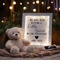 a teddy bear sitting next to a lit up sign that says, we have been keeping a little secret we are expecting june 22