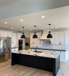 a large kitchen with an island in the middle and two pendant lights hanging from the ceiling