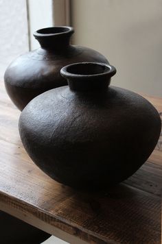 two black vases sitting on top of a wooden table in front of a window