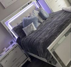 a bed with blue and white pillows on top of it in a bedroom next to a dresser