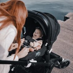 a woman looking at a baby in a stroller next to the water with her mother