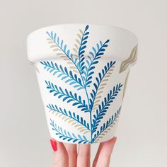 a woman's hand holding up a blue and white cup with leaves painted on it