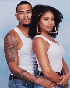 a man and woman standing next to each other in front of a blue background with tattoos on their arms