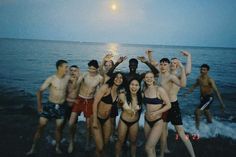 a group of people standing on top of a beach next to the ocean at night