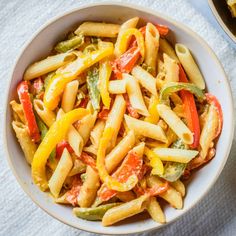 a bowl filled with pasta and vegetables on top of a white cloth next to a fork