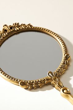 a mirror that is sitting on top of a white table with a gold frame and handle