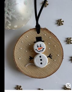 a snowman ornament hanging from a string on a wooden slice with stars around it